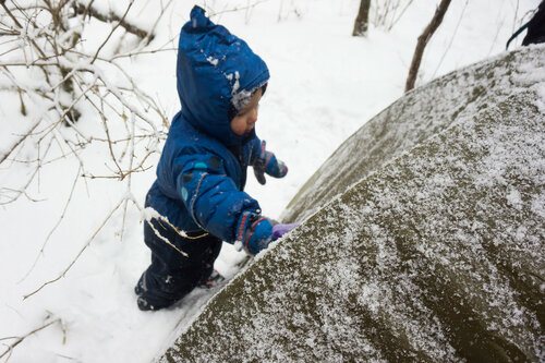 child clears snow from a tent during a winter hike